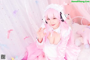 A woman with pink hair wearing headphones sitting on a bed.