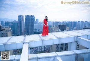 A woman in a red dress standing on a ledge.