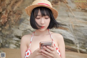 A woman in a bikini and a straw hat on a beach.