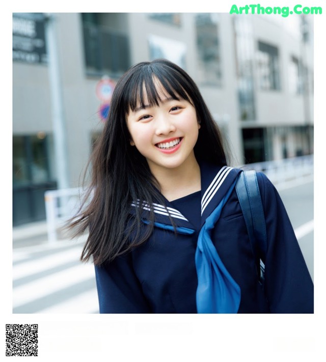 A young woman in a school uniform smiles at the camera.