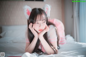 A woman in a pink outfit is sitting on a bed.