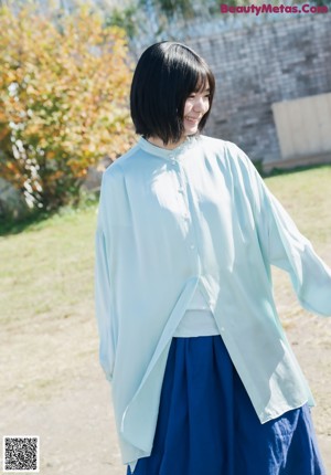 A woman in a blue shirt and green skirt holding hands with a child.