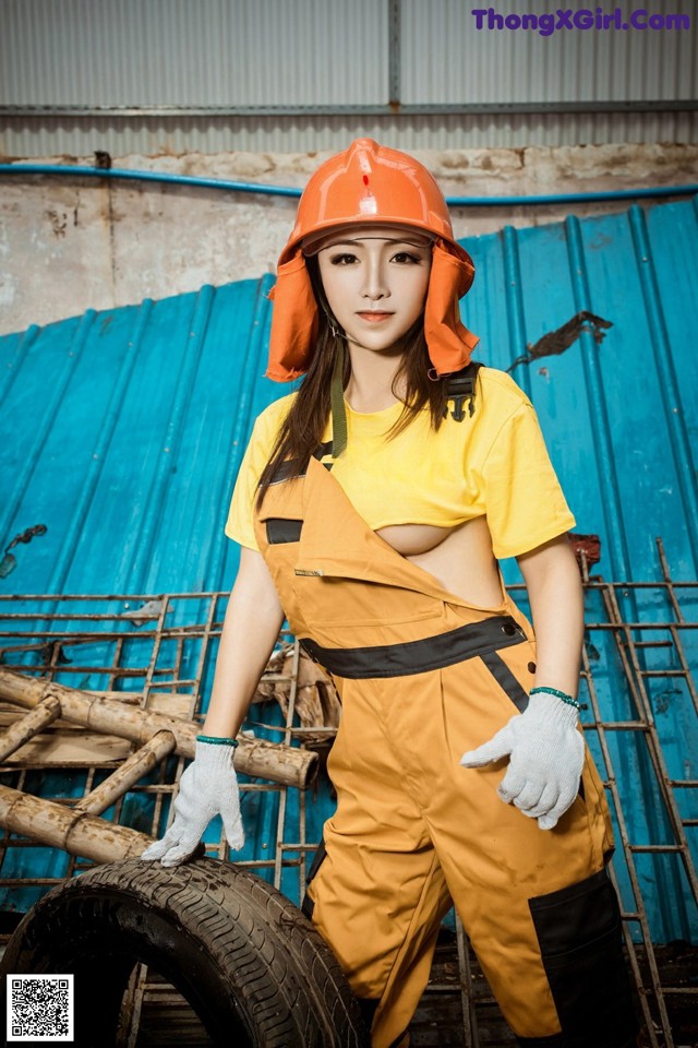 A woman wearing a hard hat and overalls posing for a picture.