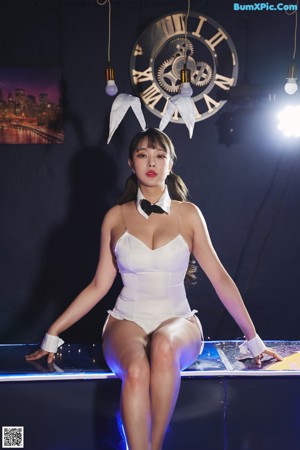 A woman in a white bodysuit sitting on a blue couch.