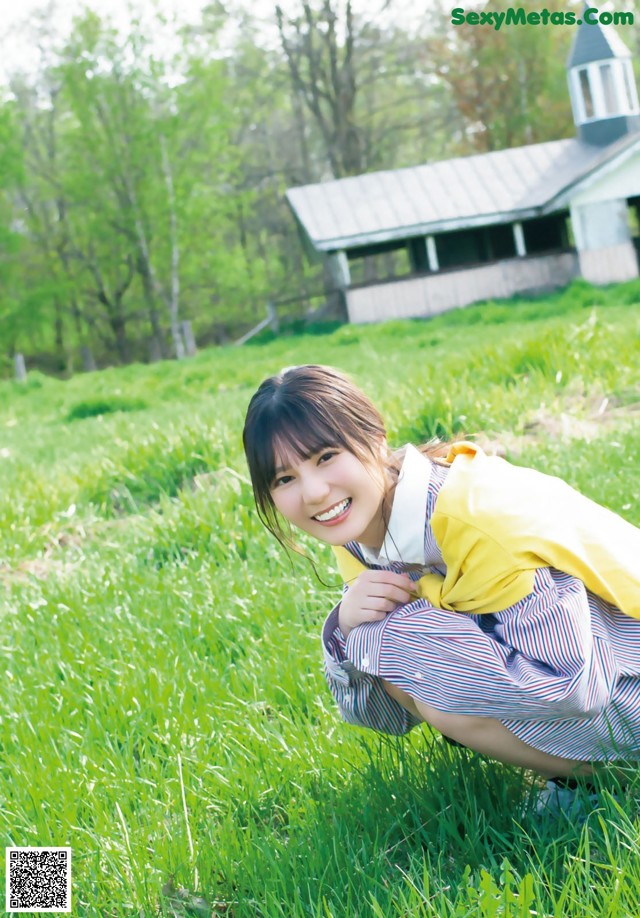 A woman in a school uniform crouching in the grass.