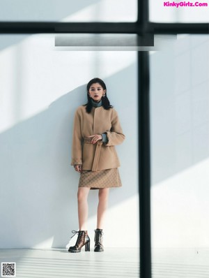 A woman standing in front of a window wearing a black coat.