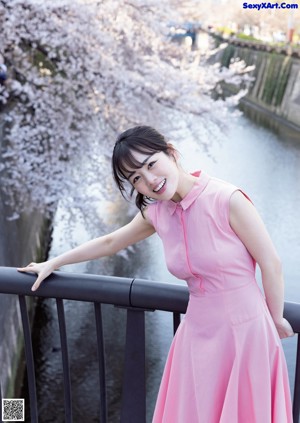 A woman in a red dress standing on a rock by the ocean.