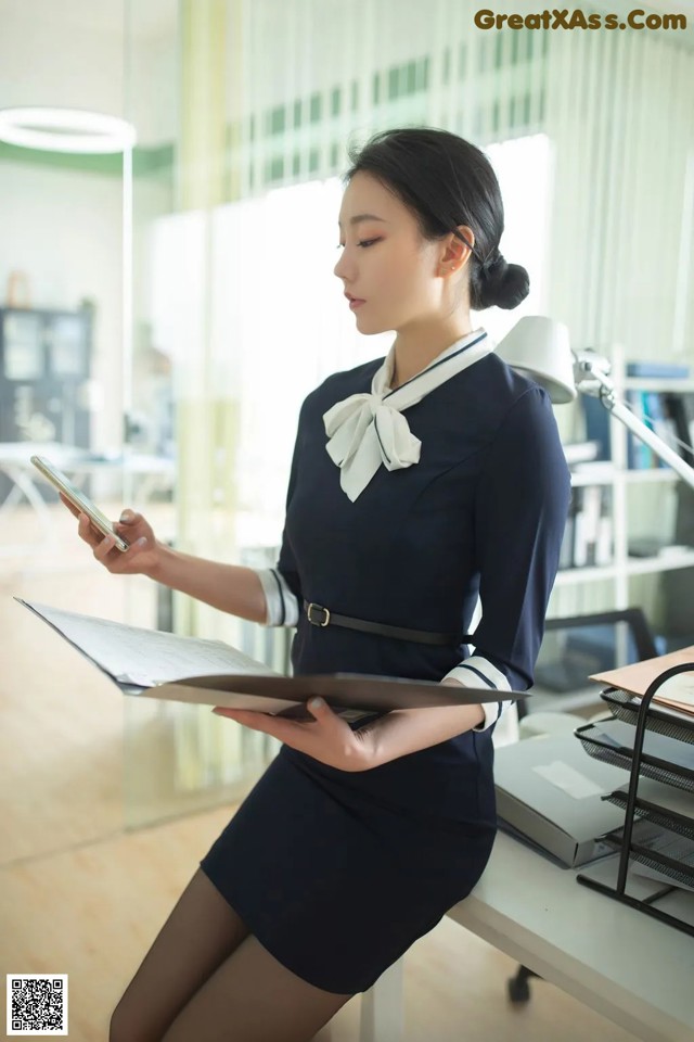 A woman sitting at a desk holding a clipboard and a cell phone.