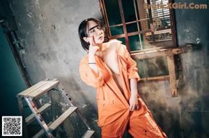 A woman in an orange jumpsuit leaning on a ladder.