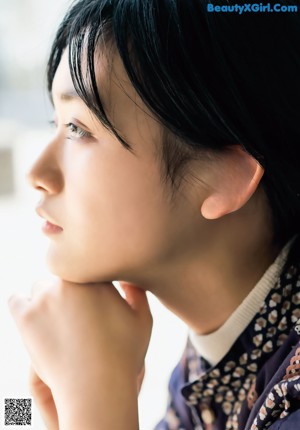 A young woman leaning on a rock with her hand on her chin.