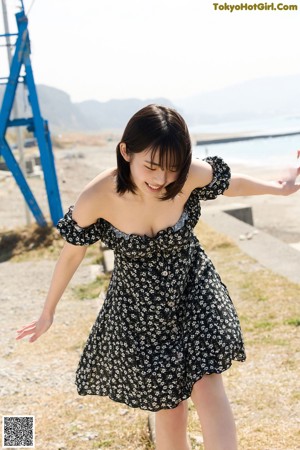 A woman in a black and white dress leaning against a wooden fence.